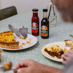 Bottles of Tomato and Worcestershire Sauces on table with plates of food