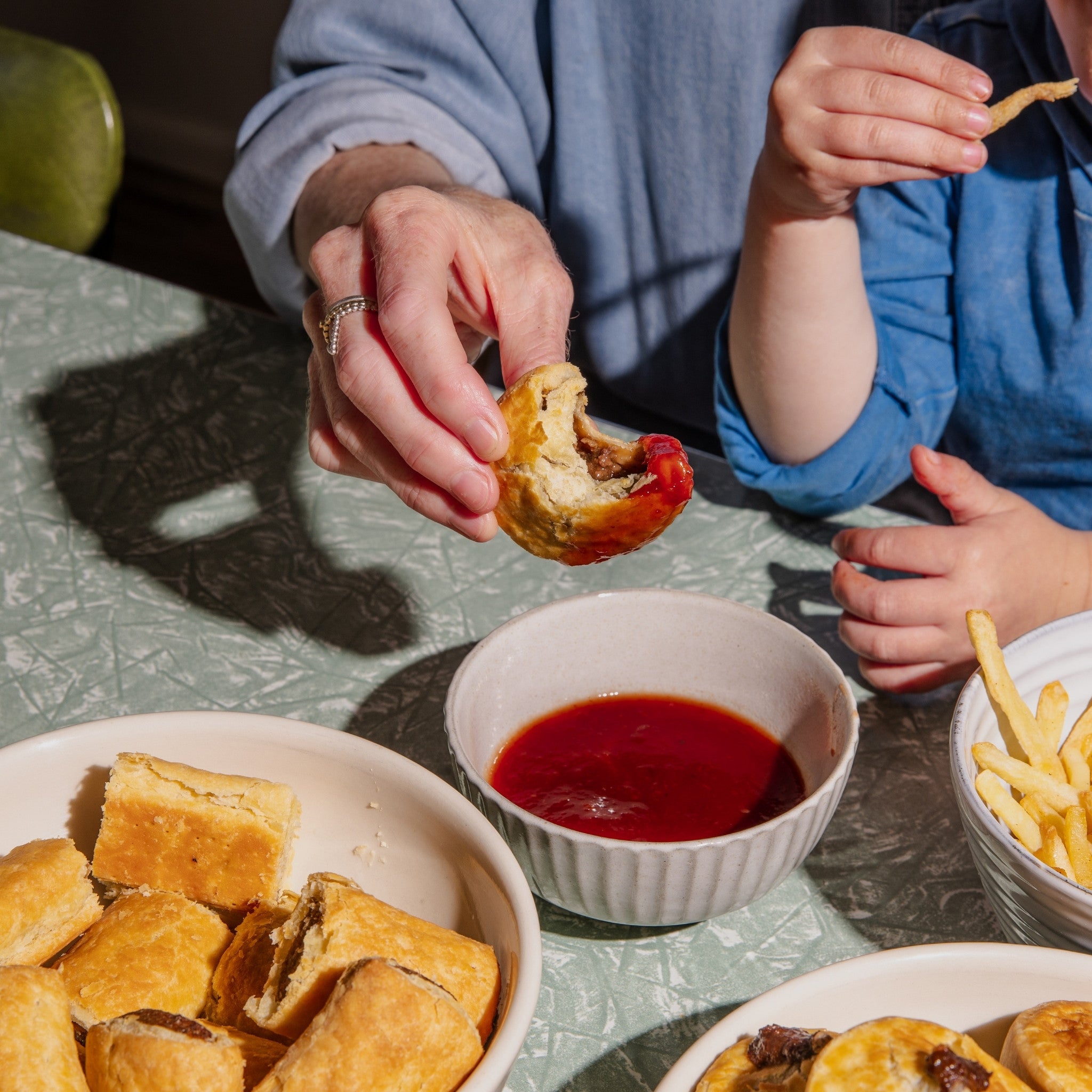 Two people eating food with a bowl of red sauce on a table.