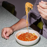 Person eating spaghetti from a bowl with a fork, sitting at a table.