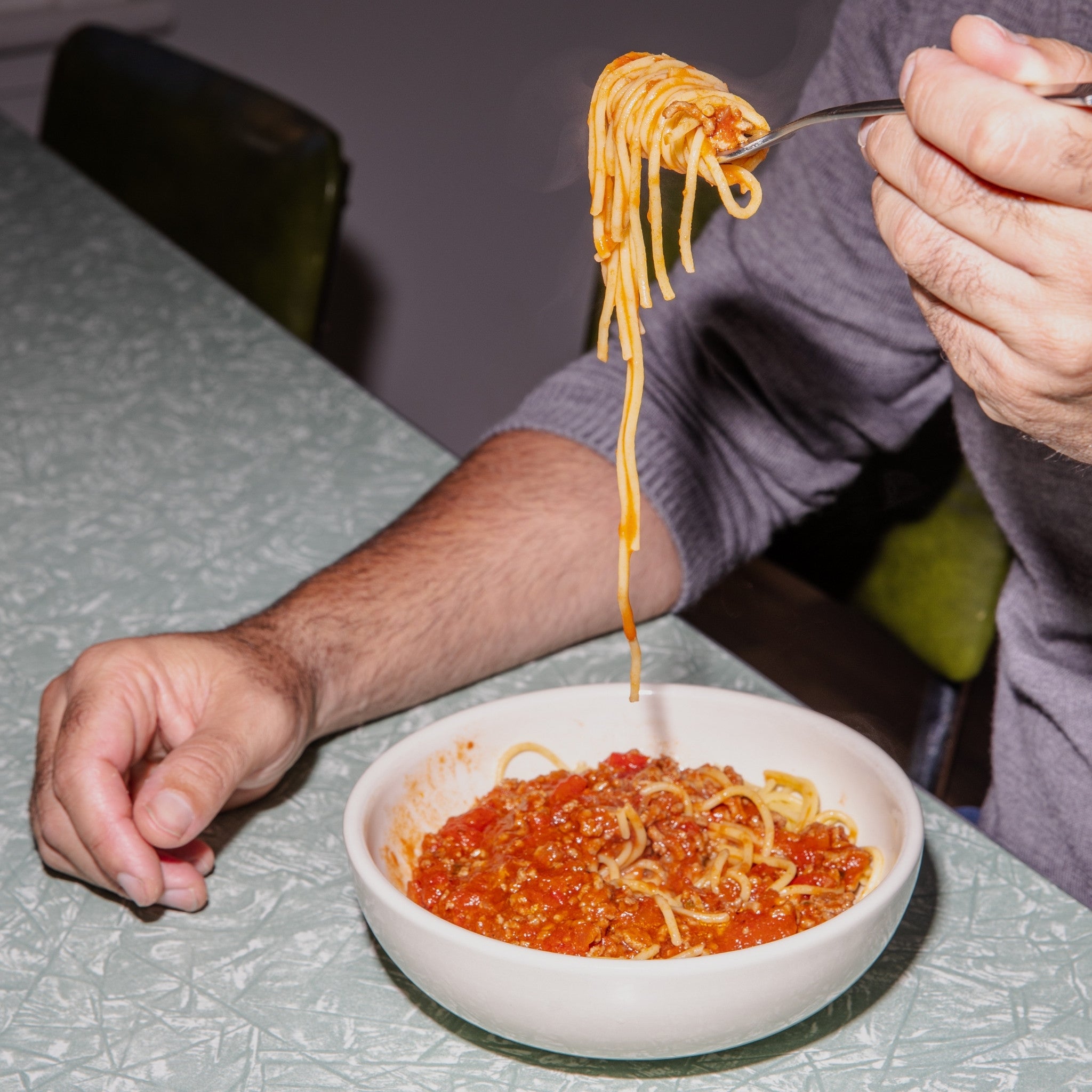 Person eating spaghetti from a bowl with a fork, sitting at a table.