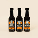 Three bottles of Corporal Freddie's Worcestershire sauce on a beige background