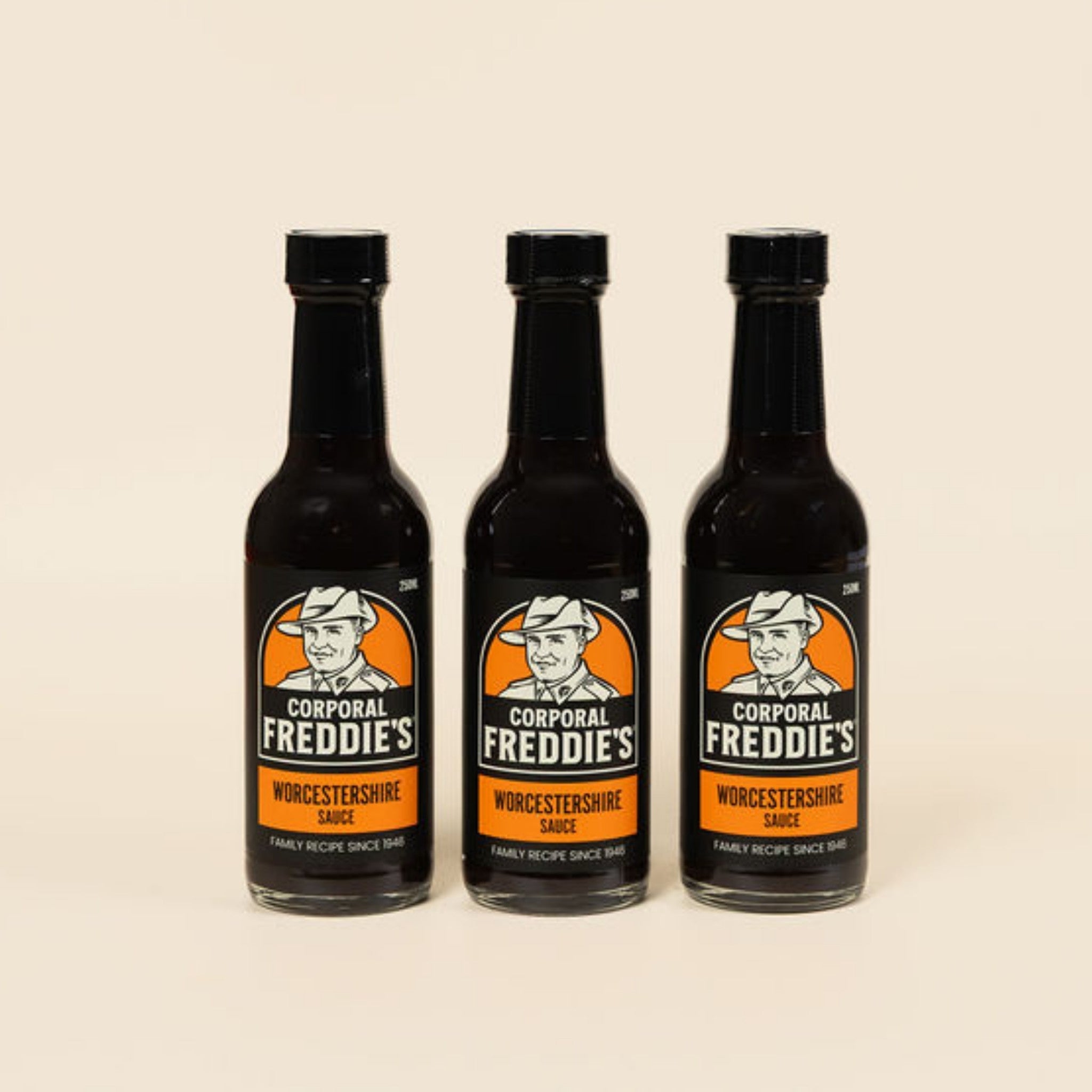 Three bottles of Corporal Freddie's Worcestershire sauce on a beige background