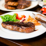 Steak with worcestershire sauce being poured onto it on a white plate with a blurred background
