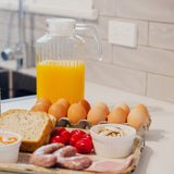 Breakfast spread with eggs, bread, tomatoes, and a pitcher of orange juice on a kitchen counter.
