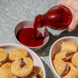 Person pouring red sauce from a bottle into a bowl with pastries on a textured surface