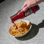 Hand pouring Freddie's Tomato sauce onto a bowl of fries