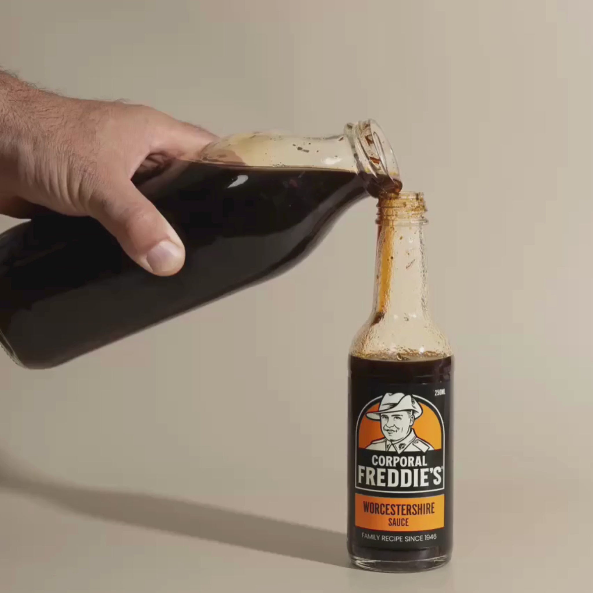 big bottle of worcestershire being poured into a small bottle of Corporal Freddie's worcestershire