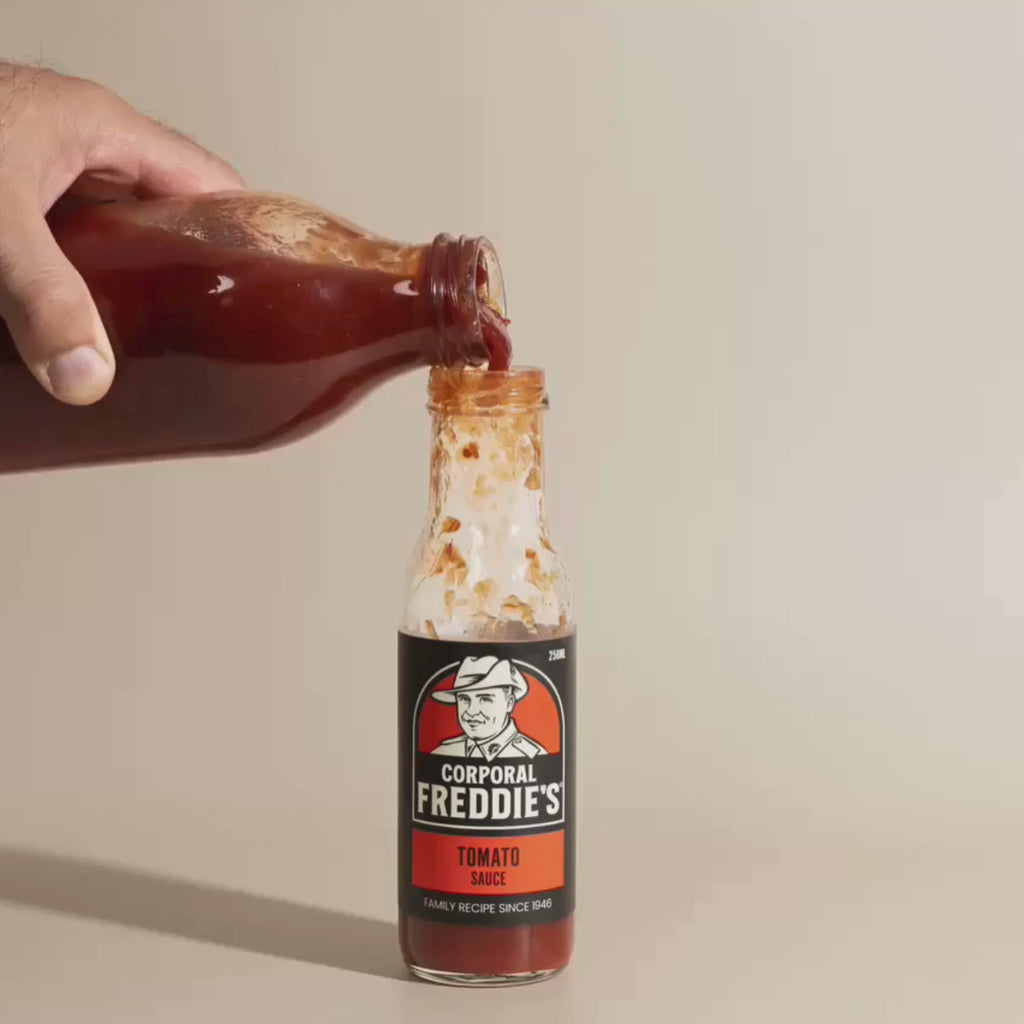 big bottle of tomato sauce being poured into small bottle of corporal freddie's tomato sauce bottle